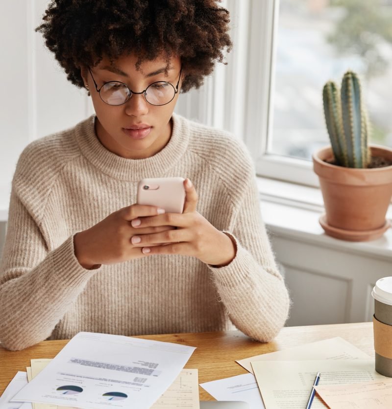 busy-businesswoman-with-afro-hairstyle-works-with-documentation-checks-bank-account-via-cell-phone.jpg